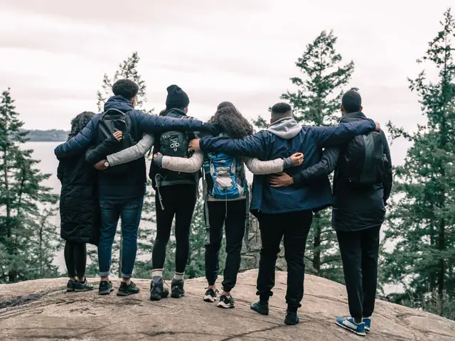 Grupo de amigos abraçados, de costas, olhando a paisagem do alto de uma pedra